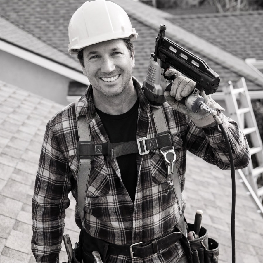 Charles Barr Jr., President of CDL Roofing, in a hard hat and safety harness holding a nail gun on a roof